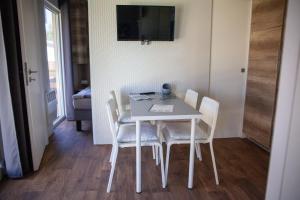 a dining room table with white chairs and a television at Oppen-House Apartmanok in Tiszafüred