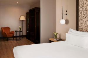um quarto com uma cama branca e uma cadeira em NH Collection Sevilla em Sevilha