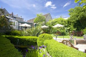 um jardim com arbustos e guarda-sóis e um lago em The Bay Tree Hotel em Burford