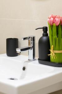 a bathroom sink with a soap dispenser and pink tulips at Apartment Tulip in Varna City