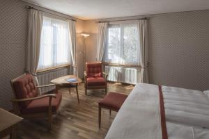 ein Hotelzimmer mit einem Bett, Stühlen und Fenstern in der Unterkunft Hotel Post in Bivio