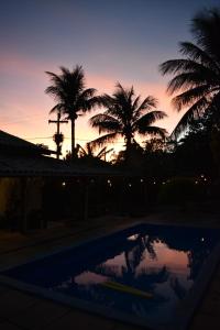 a sunset with palm trees and a swimming pool at Solar Hostel Búzios in Búzios