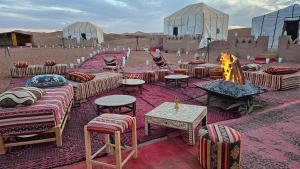 a desert encampment with couches and chairs and a fire at Nejma luxury camp erg chegaga in El Gouera
