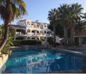 a large house with a swimming pool and palm trees at Apartamento en Cala en Porter Menorca in Cala'n Porter