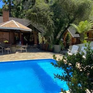 uma piscina azul com cadeiras e uma casa em Pousada Serras De Monte Verde em Monte Verde