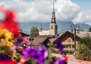 梅傑夫的住宿－Mamie Megève，一座教堂,教堂在一座鲜花盛开的小镇上,有陡峭的陡峭壁