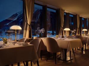 un comedor con mesas y sillas blancas y ventanas en Precise Tale Seehof Davos, en Davos