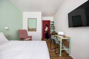 een slaapkamer met een bed, een bureau en een televisie bij Sirkin 16 Hotel - Autonomous hotel in Giv‘atayim