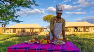un hombre está de pie junto a una mesa con comida en Serengeti Malaika Luxury Camp, en Parque Nacional del Serengeti