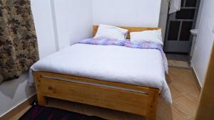 Cama pequeña con sábanas y almohadas blancas en Meru Farm House, en Arusha
