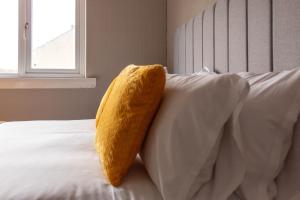 uma almofada amarela sentada em cima de uma cama branca em Linwood House em Paisley