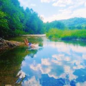 a person swimming in a river with clouds in the water at Stara Khata Карпати in Sheshory