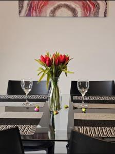 a vase of red tulips sitting on a table with glasses at Ruby Heaven Apartment in St Paul's Bay