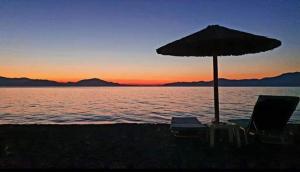 zwei Stühle und ein Sonnenschirm am Strand bei Sonnenuntergang in der Unterkunft Drosia Studios - Λυμπερόπουλος in Pefki