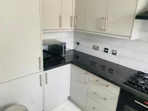 a kitchen with white cabinets and a black microwave at New Malden, 3 Bedroom Guest House in Malden