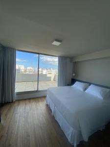 a bedroom with a white bed and a large window at Hotel Ciudadano Suites in Montevideo
