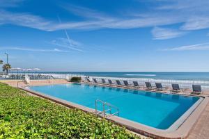 a swimming pool with chairs and the ocean in the background at Spark by Hilton Ormond Beach Oceanfront in Ormond Beach