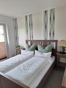 a large bed with white sheets and green pillows at Kleines Schmuckstück - Ferienwohnung Haus in Güstrow