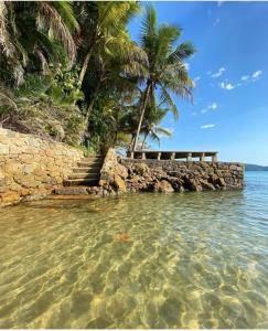 a beach with a stone wall and palm trees and the water at Pousada Mar Suites Toninhas in Ubatuba