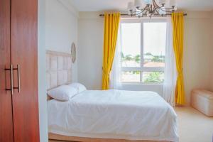 a bedroom with a bed with yellow curtains and a window at Summer in Garuga in Entebbe