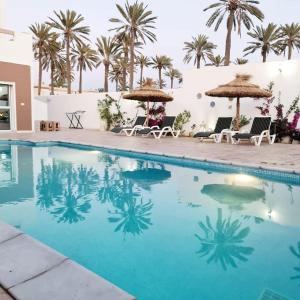 una piscina con sillas, sombrillas y palmeras en Dar selim en Midoun