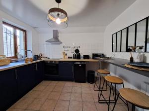una cocina con armarios negros, mesas y taburetes en L'Echappée Morétaine - Cœur de Moret, en Moret-sur-Loing