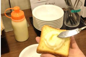 a person holding a piece of bread with a fork and butter at Dormy Inn Express Koriyama in Koriyama