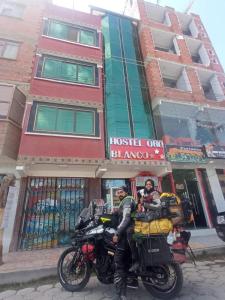 due persone sedute su una moto di fronte a un edificio di HOTEL ORO BLANCO a Uyuni