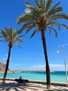 a man sitting on a bench next to two palm trees at Casita Bonita - with private garden near beach in Jávea in Jávea