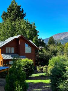 a wooden house with trees and mountains in the background at Cabañas El Refugio de Puelo in Lago Puelo