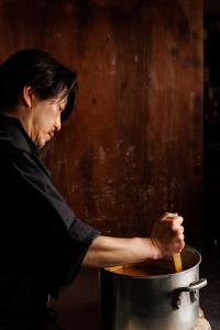 una mujer revolviendo una olla con una cuchara de madera en Fukashiso, en Matsumoto
