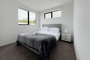 a white bedroom with a bed and two windows at Modern 3-bds townhouse in South Auckland in Auckland