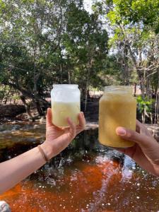 two people holding drinks in their hands in front of a stream at SÍTIO CAPÃO DO MEL in João Pessoa