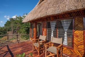 a cabin with two chairs and a thatch roof at Njobvu Safari in Kakumbi