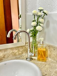 a bathroom sink with a vase of flowers and a mirror at CASA LUMEN Home Hostel in Núcleo Bandeirante