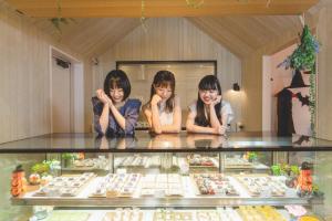 Hotel & Sweets Fukuoka LOVEHOTEL في فوكوكا: ثلاث فتيات جالسات جالسات خلف صندوق عرض للطعام