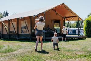 Una donna che tiene due bambini di fronte a una tenda di Luxe Safaritent voor het hele gezin I 6 personen a Epe