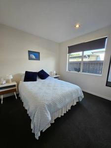 a white bedroom with a bed and a window at Golden Sands Beachside Cottage in Papamoa