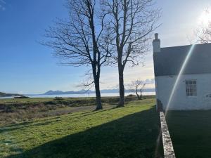 a white building with a tree next to a body of water at Clachan Manse Bed & Breakfast in Applecross