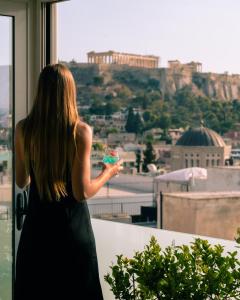 Une femme qui regarde par une fenêtre dans une ville dans l'établissement Athens Cypria Hotel, à Athènes