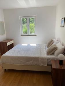 a white bedroom with a bed and a window at Apartman Emil in Supetar