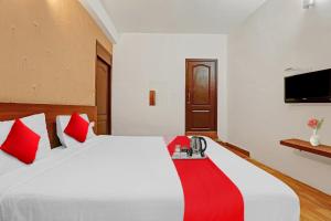 OYO Hotel Jayam Ooty Residency في أوتي: غرفة نوم مع سرير أبيض كبير مع وسائد حمراء