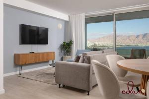uma sala de estar com um sofá, uma televisão e uma mesa em דירת 2 חדרי שינה עם נוף מדהים לים - By Edom em Eilat