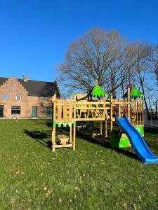 een houten speeltuin met een glijbaan in het gras bij Vakantiewoning Domein Hooverbosch in Zonnebeke