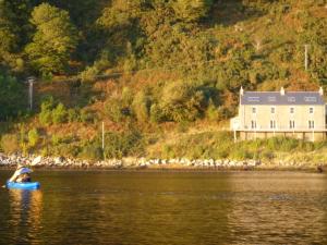 a person in a blue boat in the water with a house at Tigh na Breac - Great Outdoor Activity Location in Bonawe
