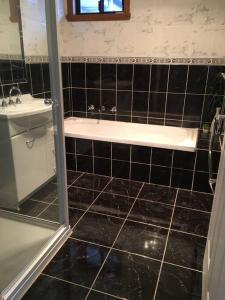 uma casa de banho com azulejos pretos, uma banheira e um lavatório. em Blackstone Lakeside 4 Bedrooms 2 Bathrooms em Hadspen