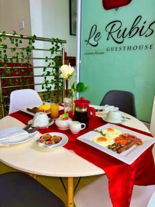 uma mesa com comida para o pequeno-almoço numa toalha de mesa vermelha em Le Rubis Guesthouse em Van Riebeekhoogte