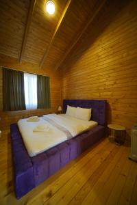 Cama en habitación de madera con sofá púrpura en Bioland VILLA's, en Novoberdo