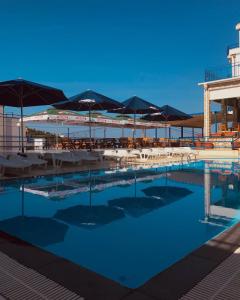 uma piscina com guarda-sóis, mesas e cadeiras em El Mar Hotel em Bar