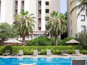 a swimming pool with chairs and umbrellas and palm trees at Novotel Dakar in Dakar